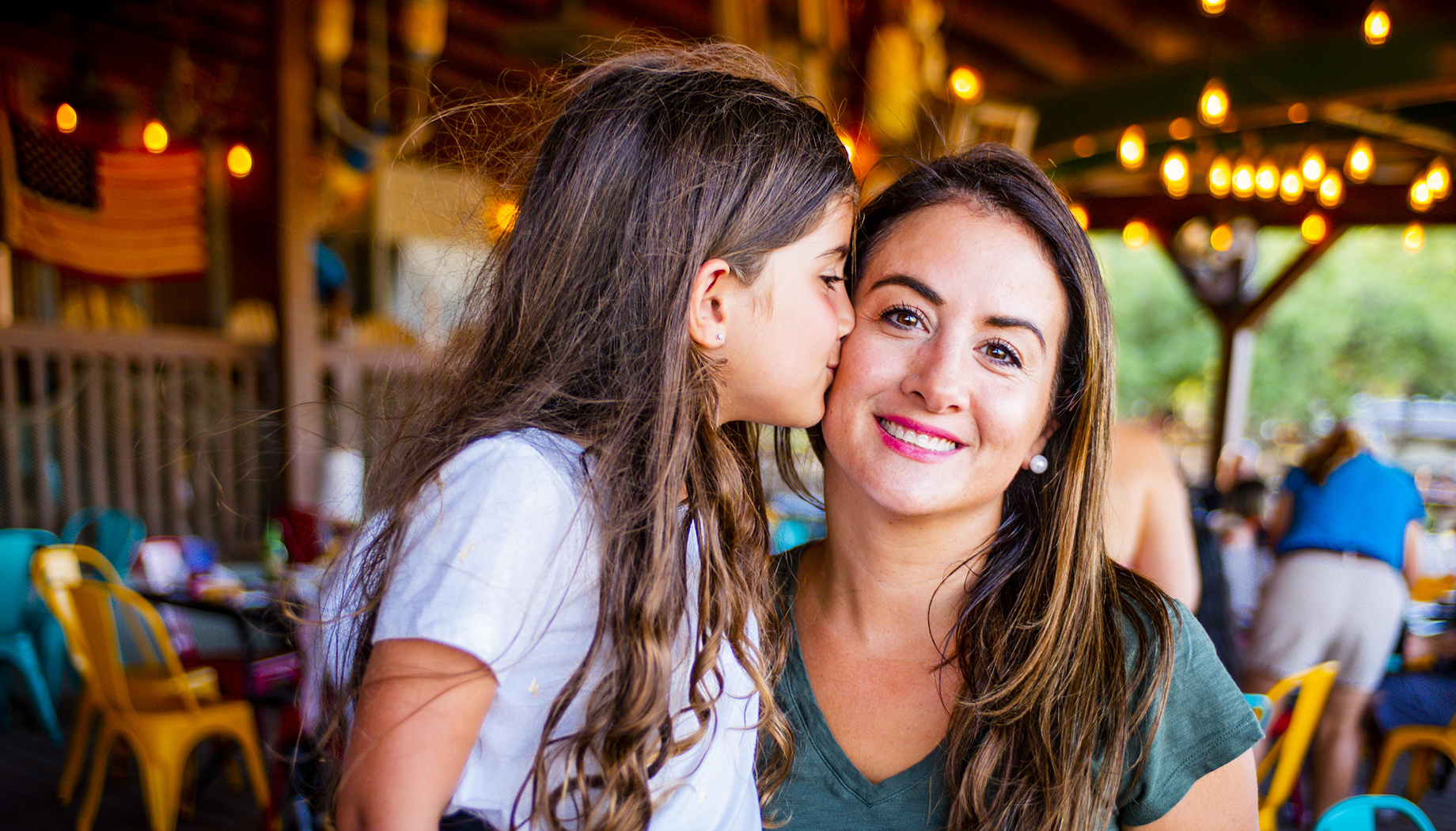 A young girl with long hair kisses a smiling woman on the cheek.